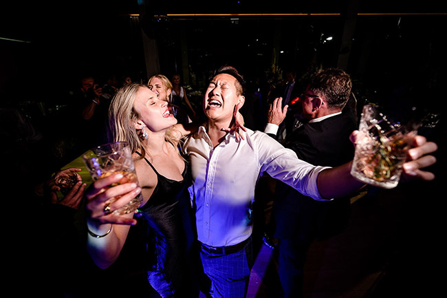 Joyful wedding guests dancing and celebrating with drinks at a lively reception.