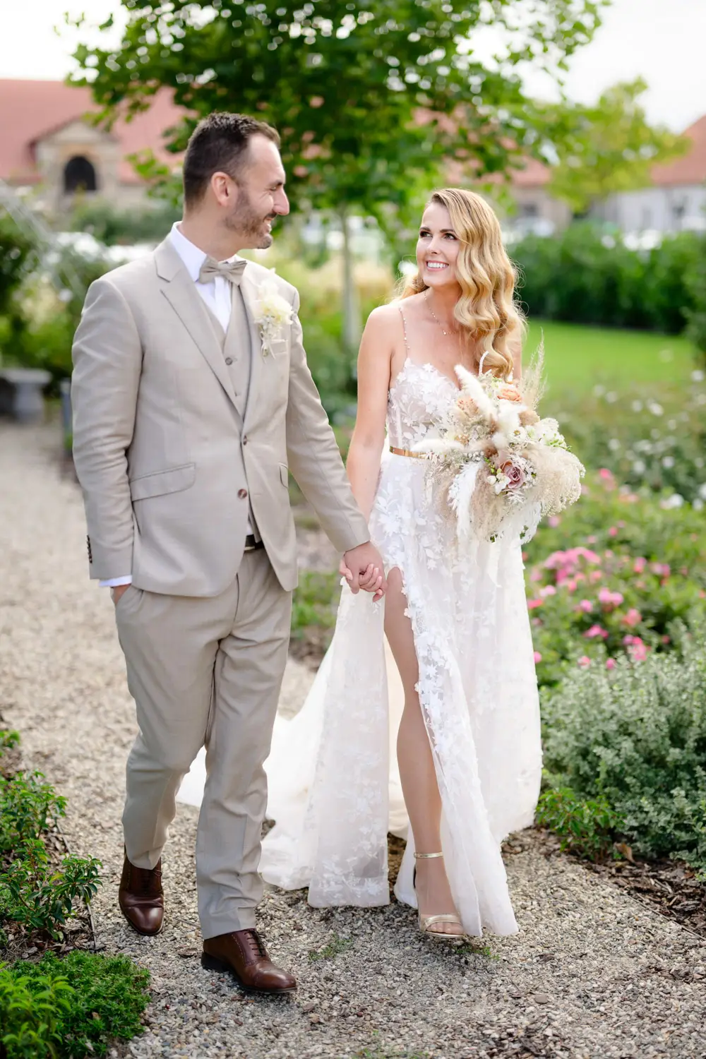 nevěsta s ženichem držící se za ruce kráčí rozkvetlou zahradou