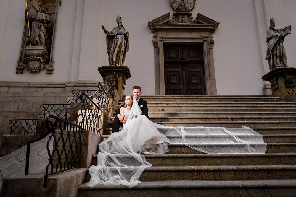 nevěsta s ženichem sedí na schodech před kostelem v Praze