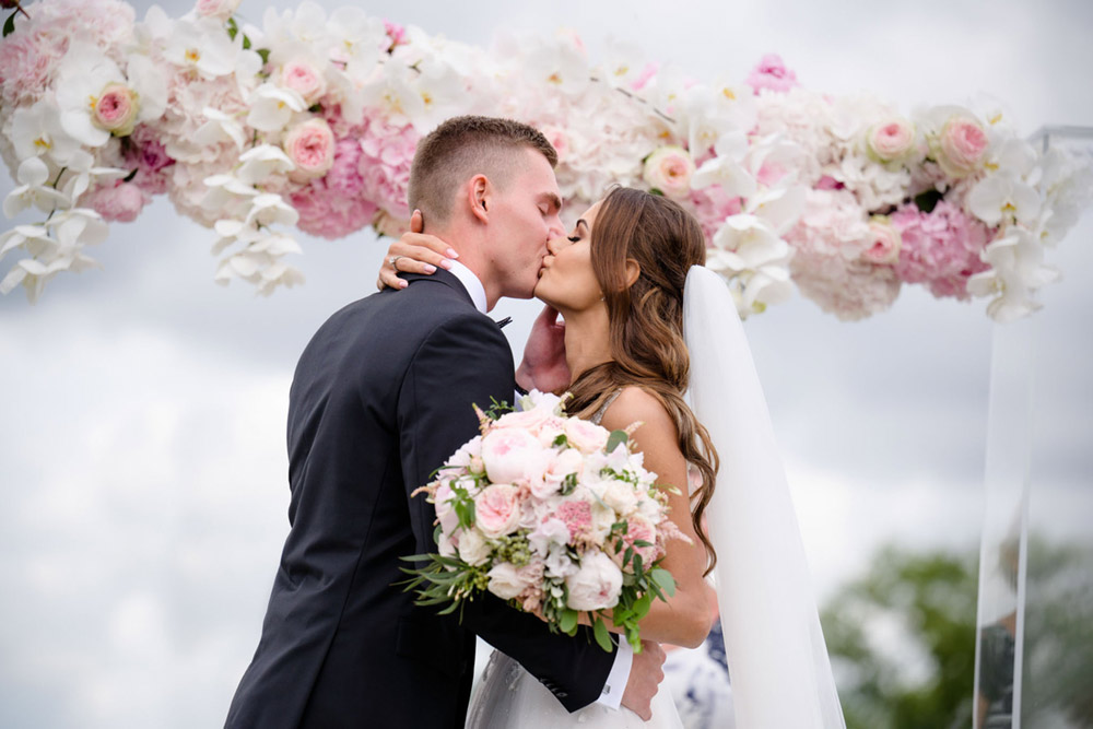 první polibek nevěsty a ženichy pod slavobránou s bohatou květinovou výzdobou v Praze