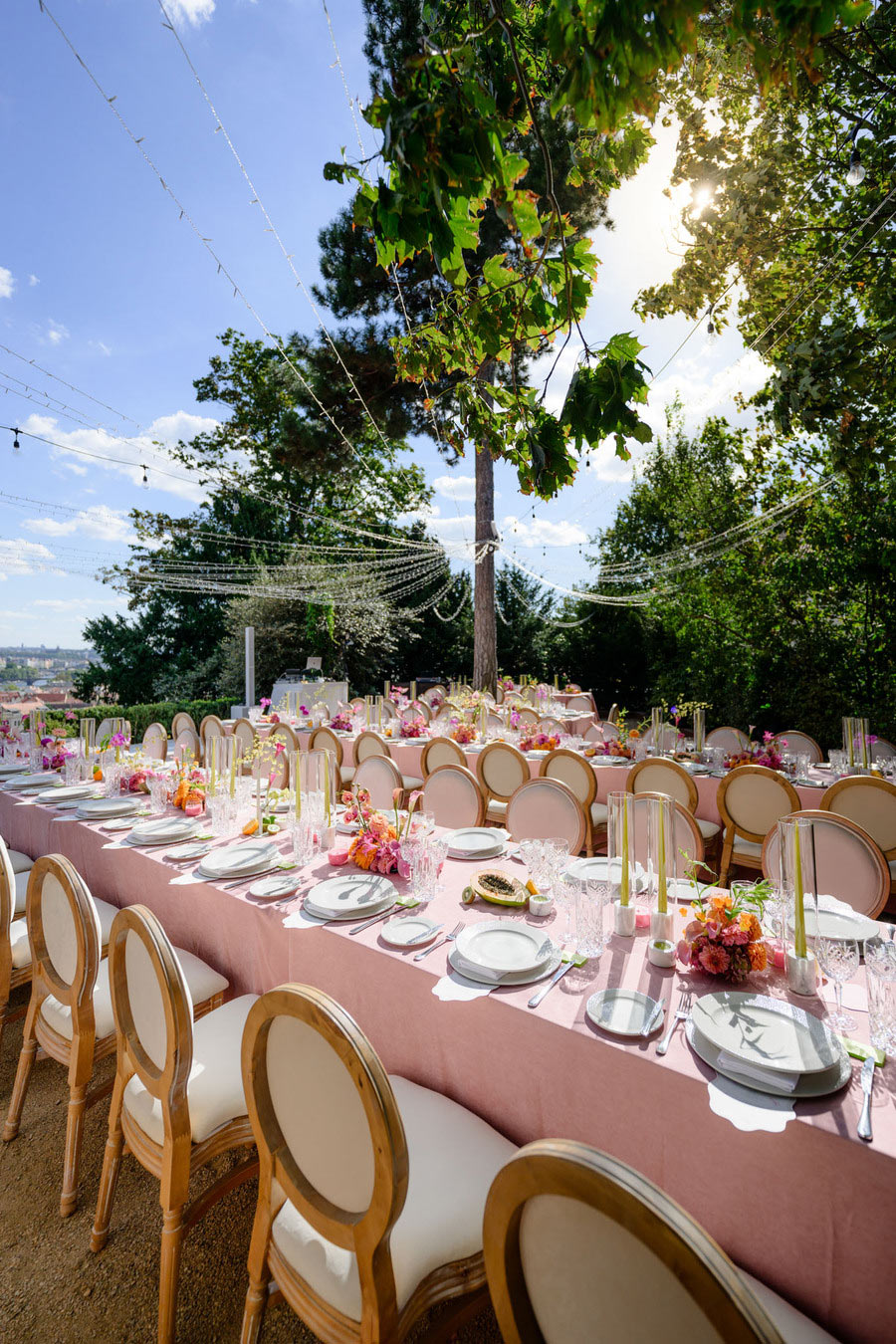 "Romantická svatební hostina ve Villa Richter u Pražského hradu – elegantní výzdoba dlouhého stolu s růžovými ubrusy, skleněnými svícny, květinovými aranžmá a zlatými židlemi.
