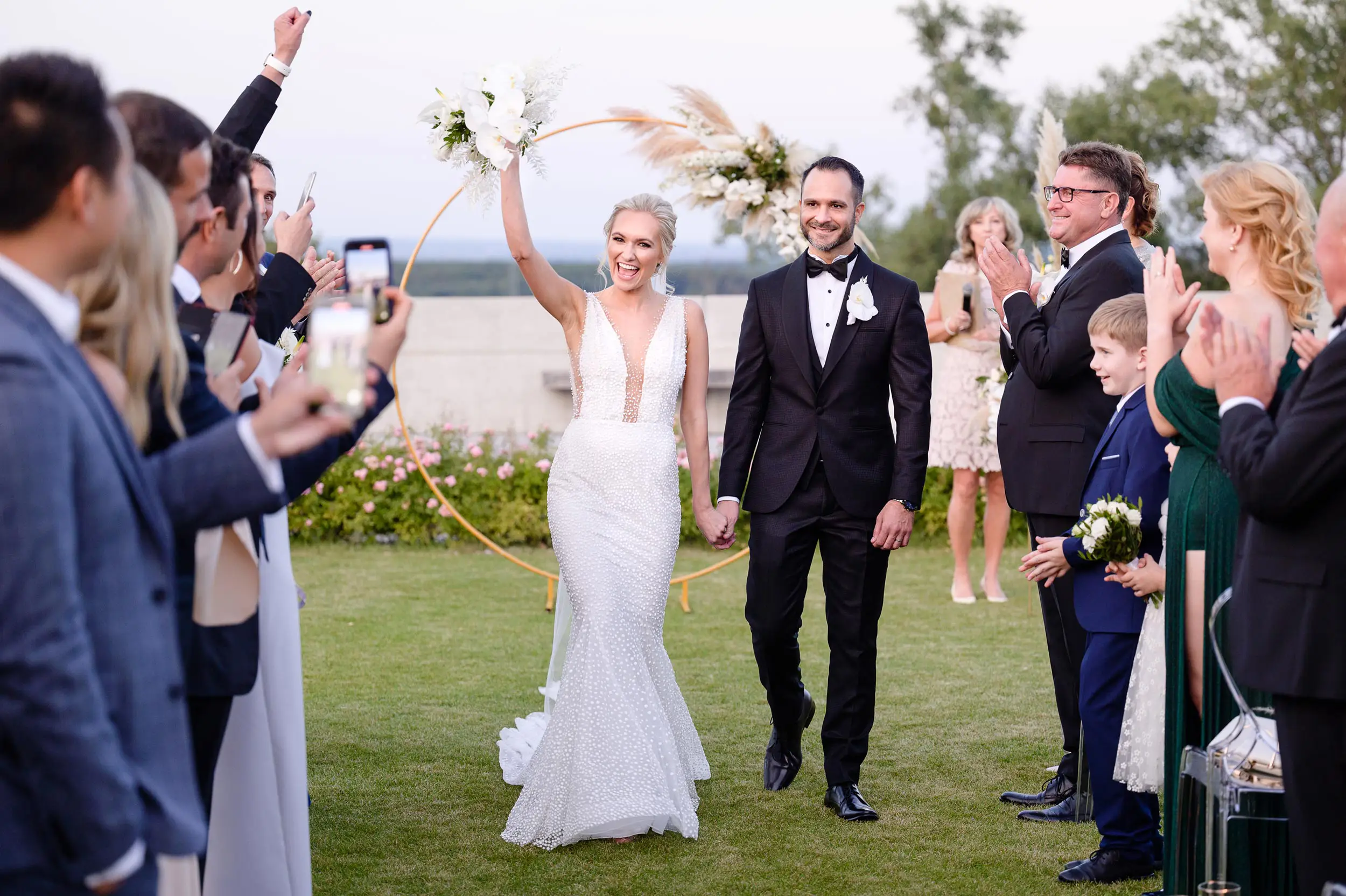 Joyful bride raising bouquet walking down the aisle with groom at a Prague wedding.