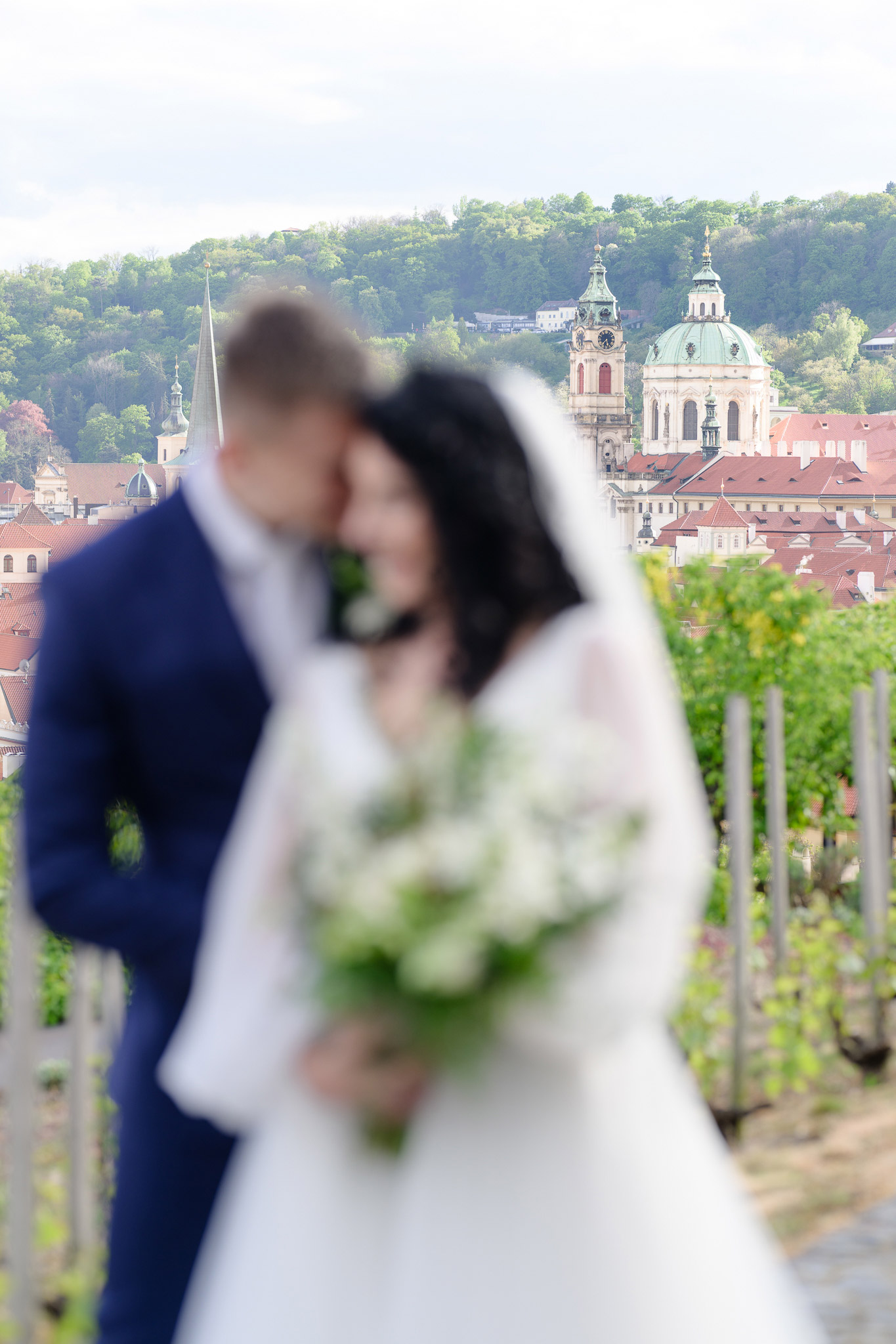 Nevěsta a ženich v obětí s panoramatem Prahy na pozadí na svatbě ve Villa Richter.