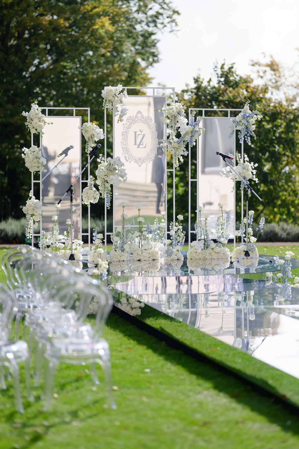 Outdoor wedding ceremony setup at Chateau Mcely with a reflective aisle, floral decorations, and transparent chairs.