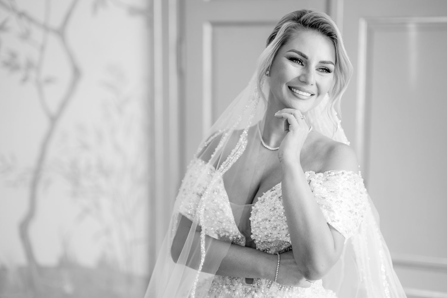 Black and white portrait of a bride smiling, wearing a detailed wedding dress and veil, posing indoors at Chateau Mcely.