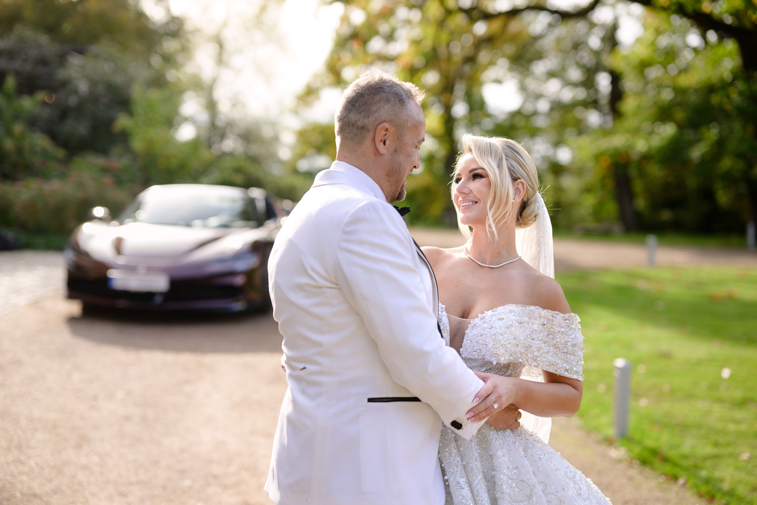 Bride and groom celebrating their wedding day at Chateau Mcely, standing together in a park with a luxury sports car in the background.