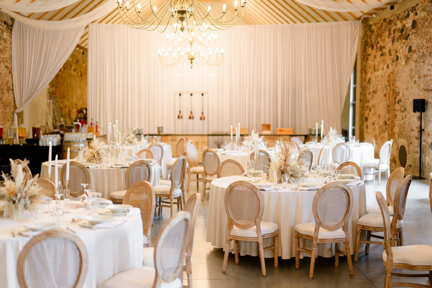 Elegant wedding setup at Na Kmíně with round tables, white drapes, and rustic stone walls