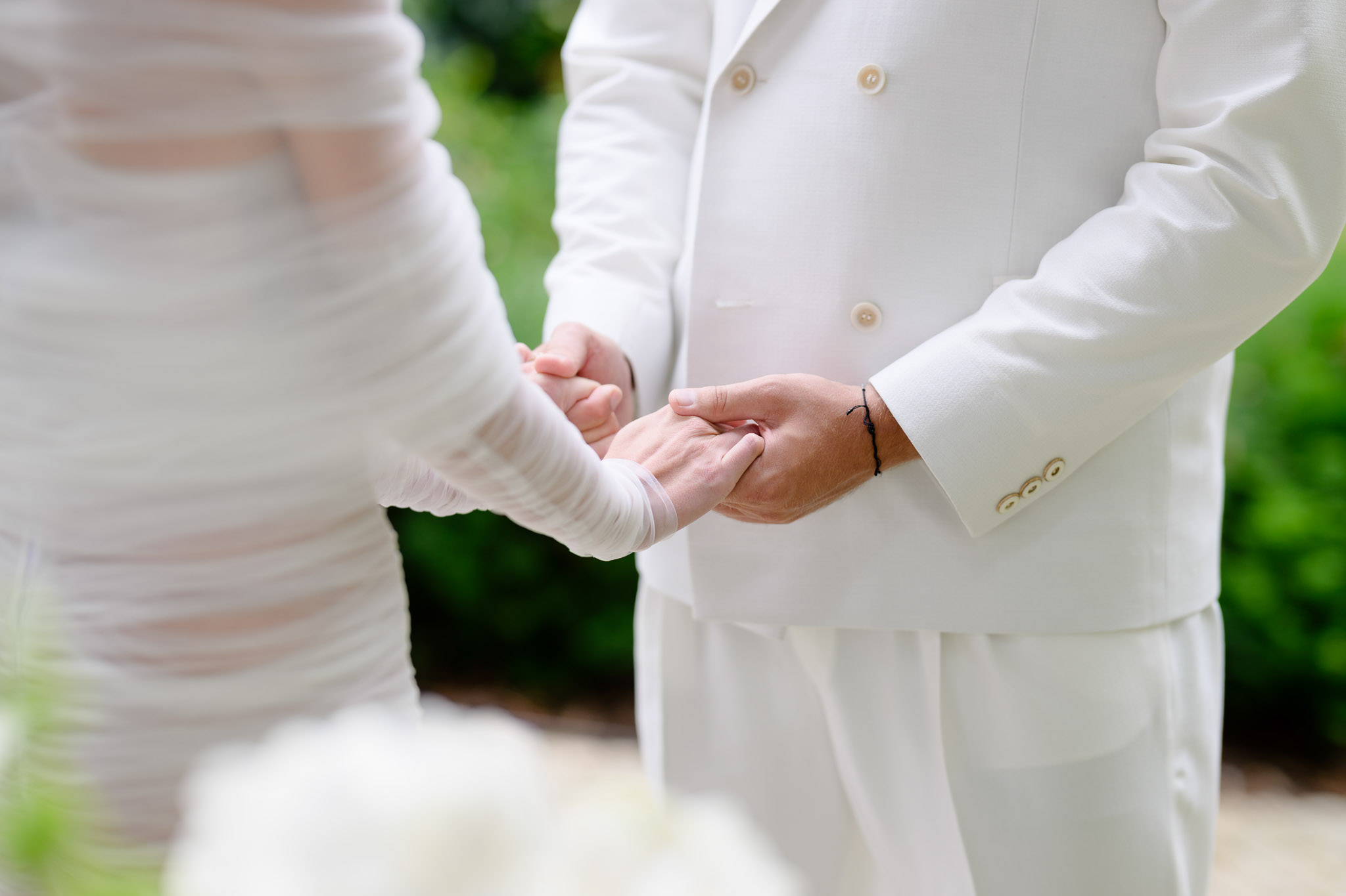Detail from Debbie Brown’s wedding ceremony in Karlovy Vary – the bride and groom in white outfits holding hands while exchanging vows.