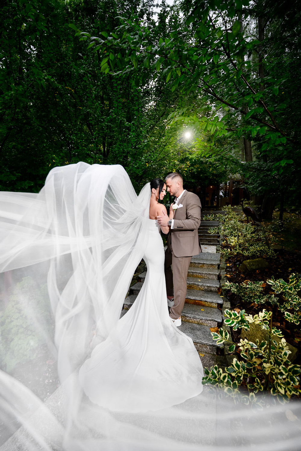 Svatební pár v resortu Cattalaya: romantický okamžik na schodech v zeleni, dlouhý svatební závoj vlaje ve vzduchu.