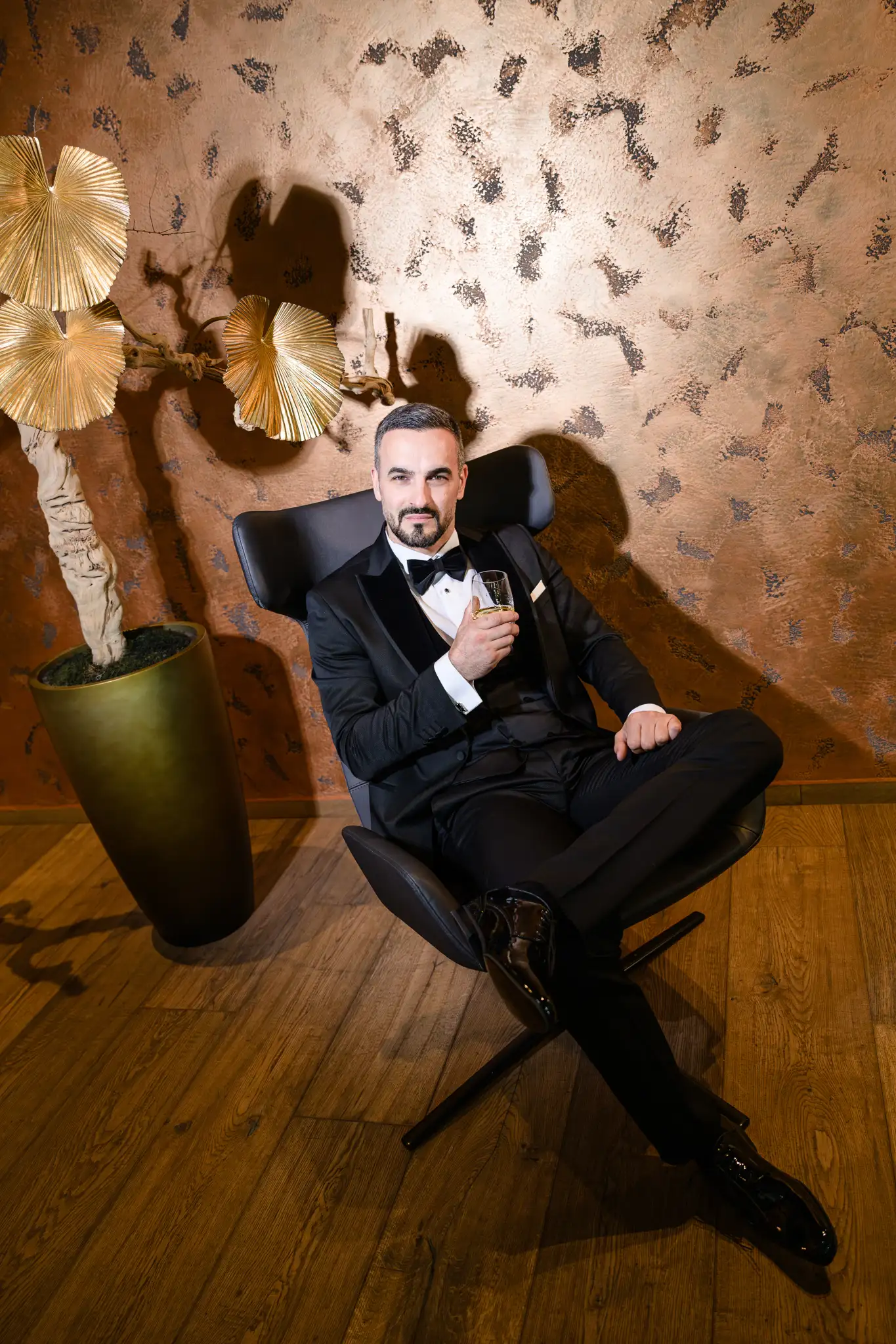 groom sitting in a chair next to a golden wall