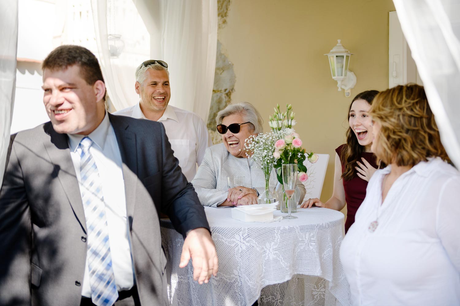 people laughing at the table with white tablecloth and flowers