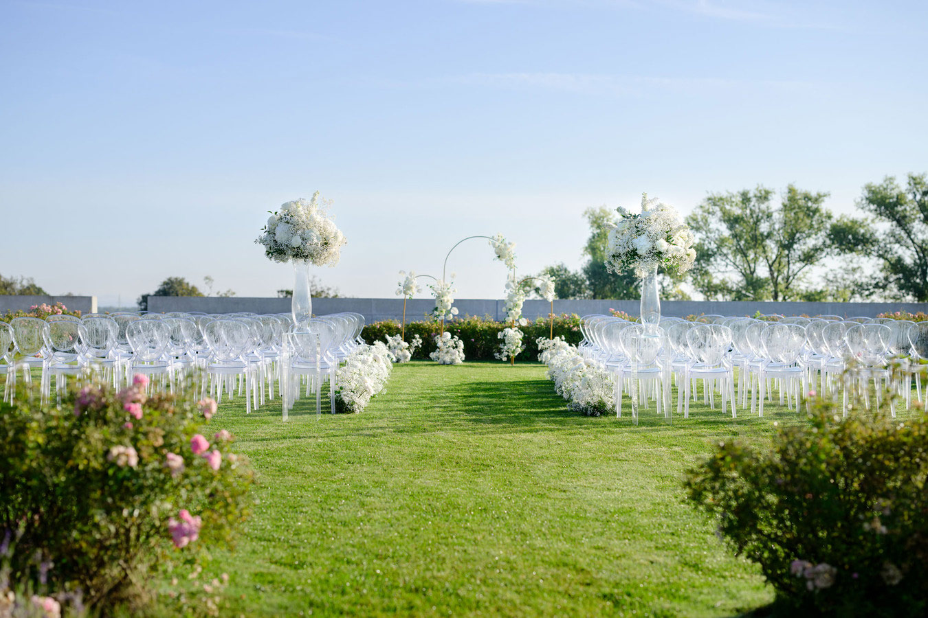Venkovní svatební obřad u Brna s elegantní bílou květinovou výzdobou a průhlednými židlemi na trávníku