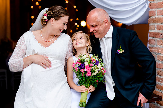 nevěsta s ženichem a dcerou držící svatební kytici se na sebe smějí