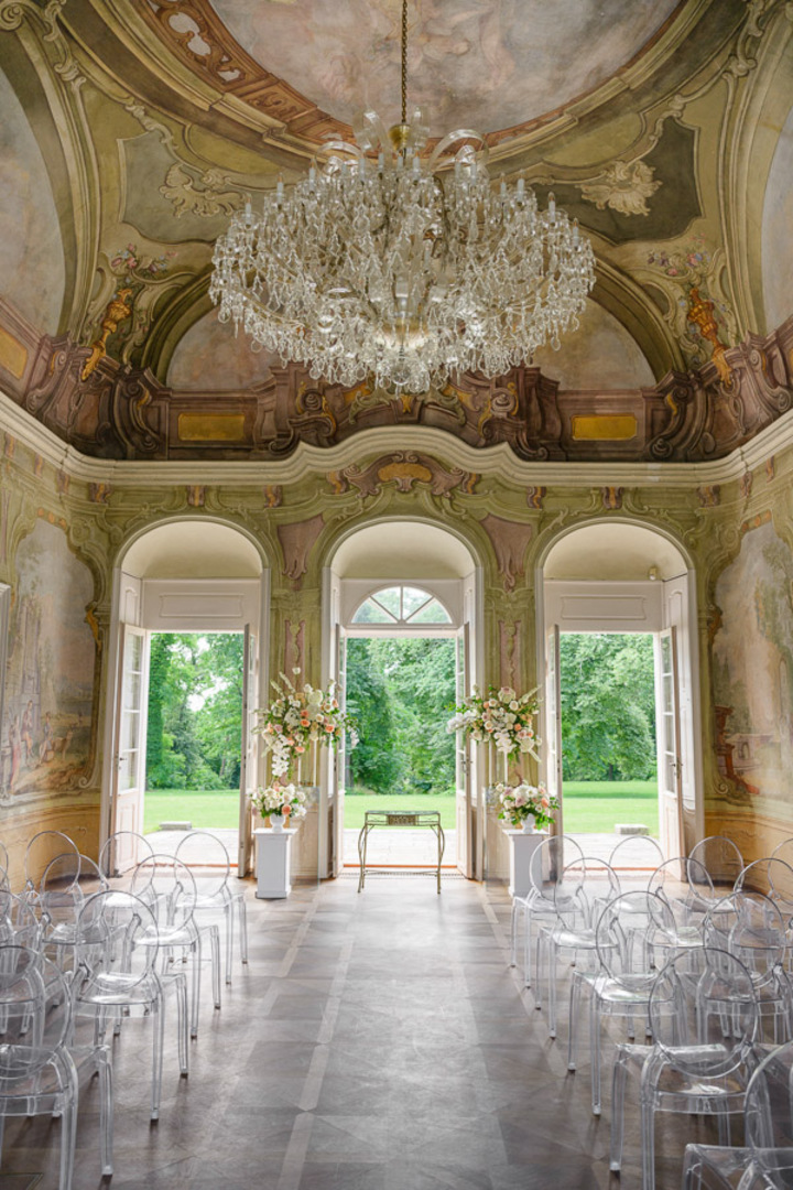 Grand chandelier and floral decorations in the opulent Bon Repos wedding venue, with transparent chairs and a scenic view.