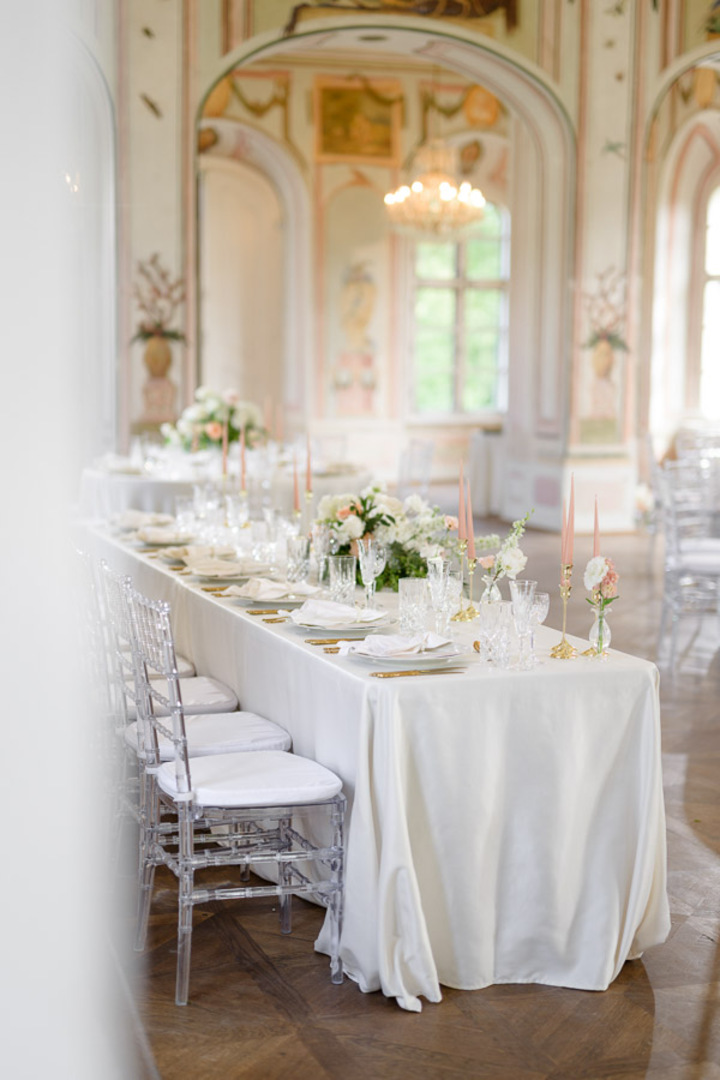 Elegant wedding reception setup at Bon Repos, featuring a long table with white linens, floral centerpieces, and clear chairs.