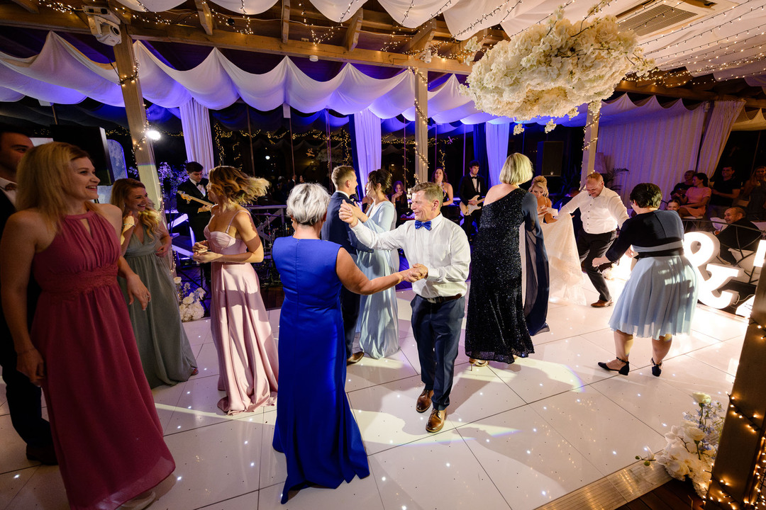 Guests in formal attire dance and celebrate on a beautifully lit dance floor at a chateau wedding reception.