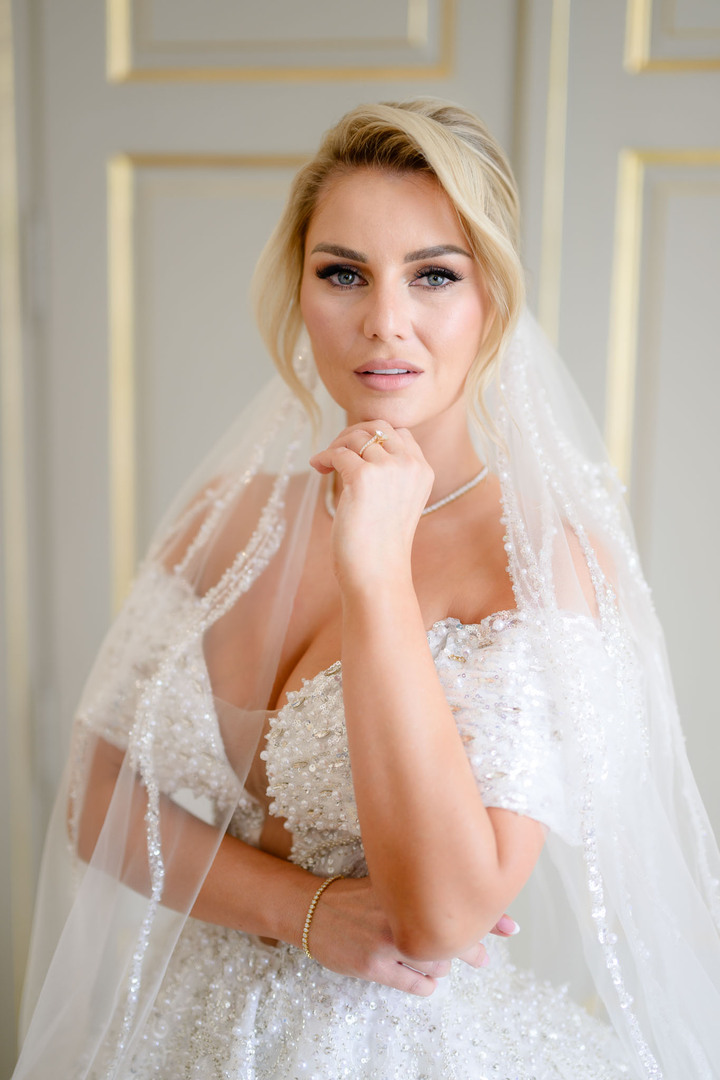 Portrait of a bride smiling, wearing a detailed wedding dress and veil, posing indoors at Chateau Mcely.