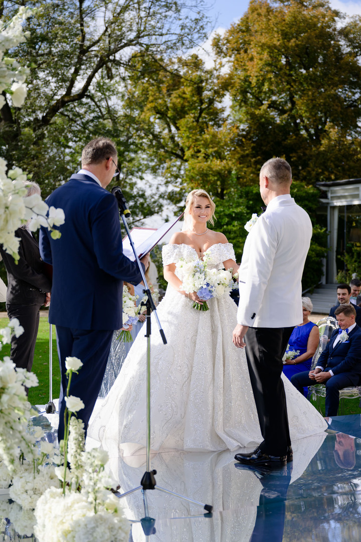 Bride smiling during a luxurious outdoor wedding ceremony at Chateau Mcely, surrounded by elegant floral arrangements and guests.