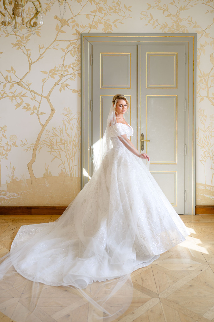 Elegant bride in a flowing white wedding gown posing gracefully in a luxurious room at Chateau Mcely.