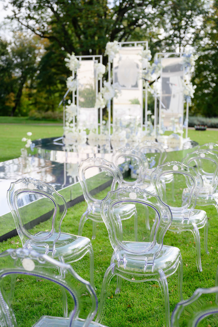 Elegant transparent chairs and floral decorations at an outdoor luxury Chateau Mcely wedding ceremony.