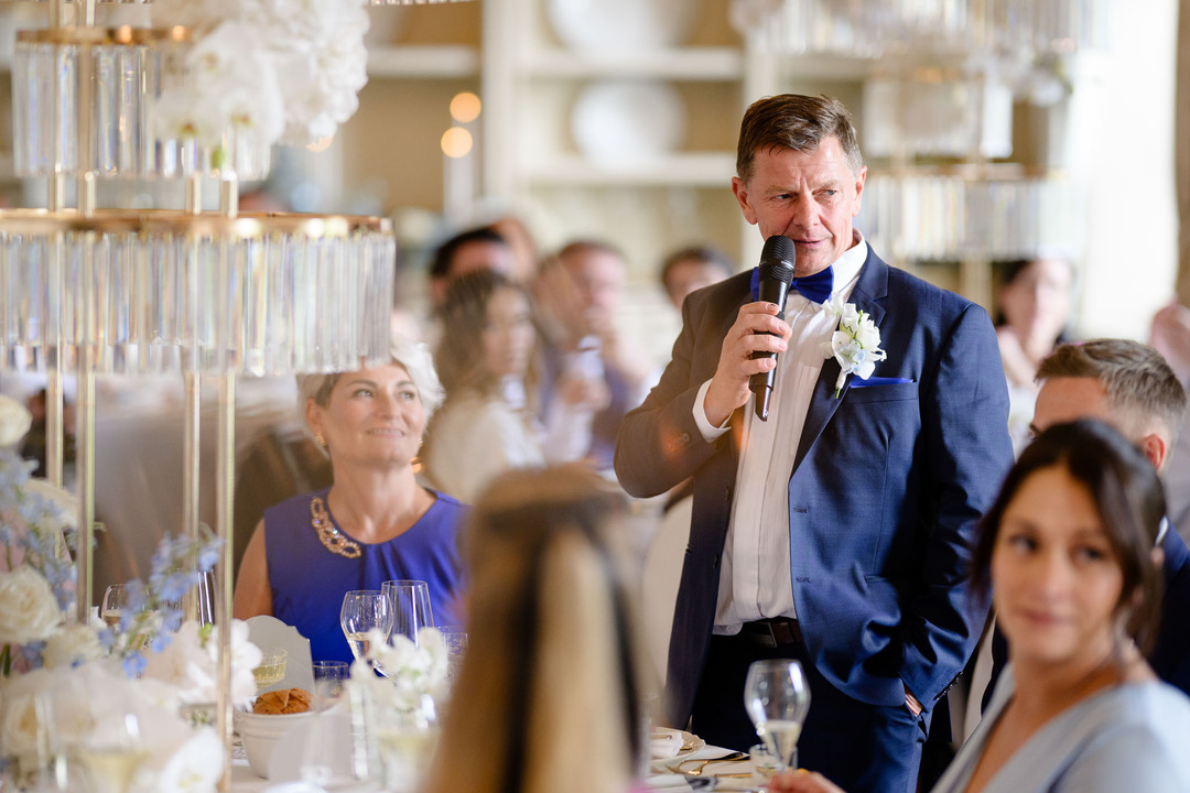 Heartfelt moment of a wedding speech being delivered at Chateau Mcely, with guests attentively listening amidst the luxurious and elegant setting of the reception.