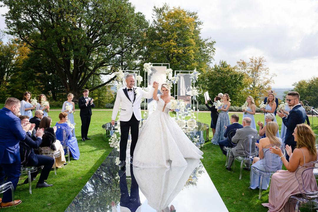 A joyful couple celebrating their wedding, raising hands in joy, with guests cheering in a beautifully decorated garden.