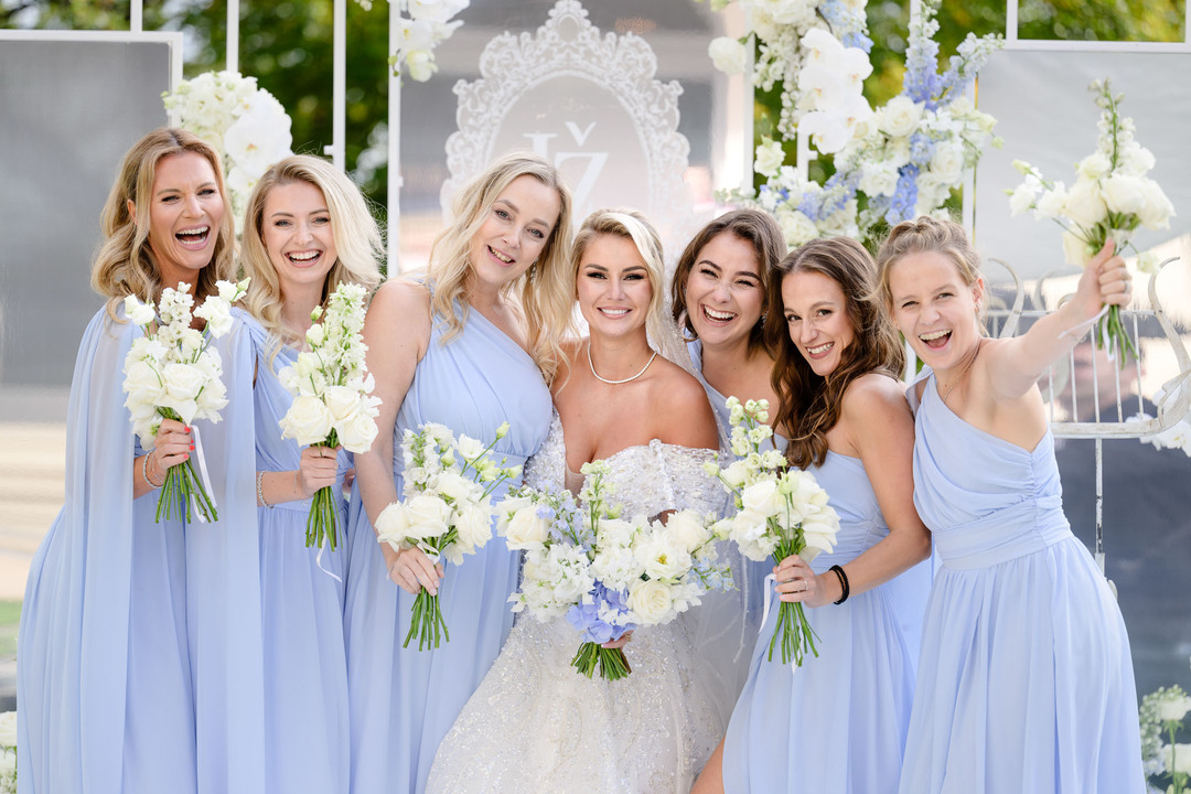 Bride with bridesmaids in light blue dresses holding white bouquets at a Chateau Mcely wedding.