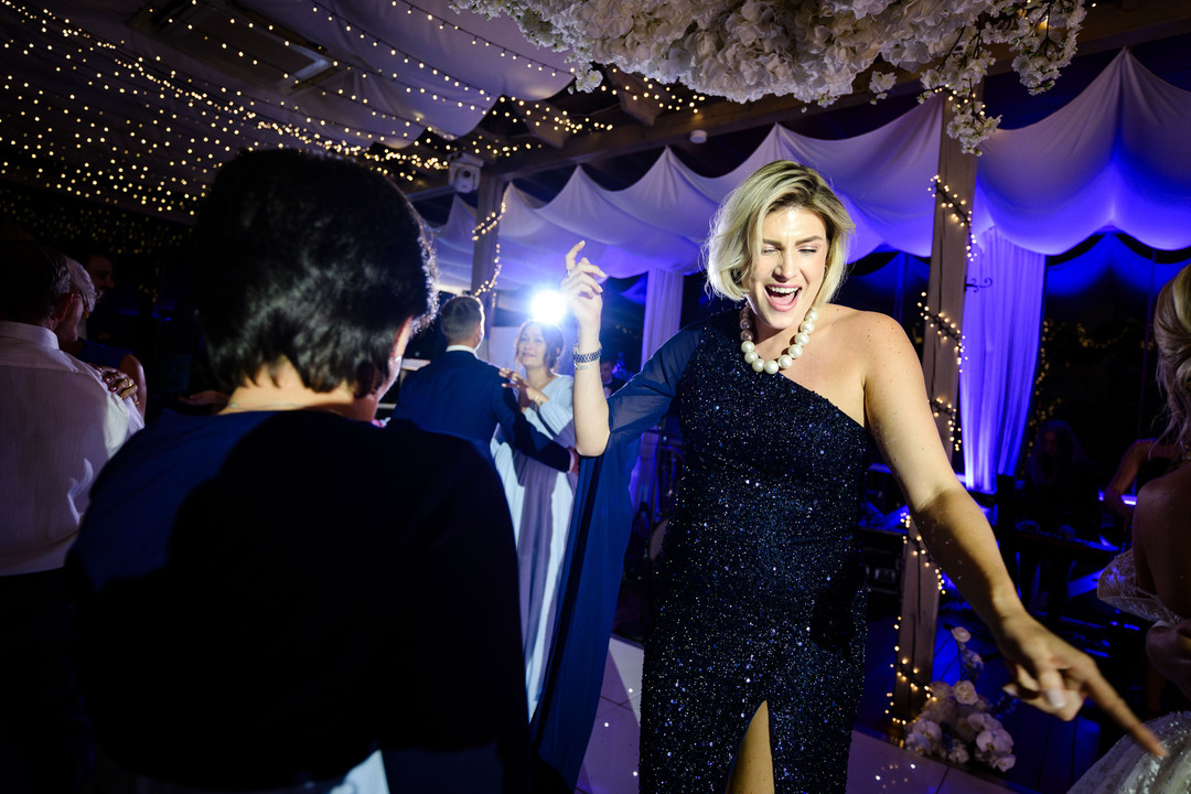 A woman in a sparkling black dress dances energetically under elegant floral decorations at a chateau wedding.