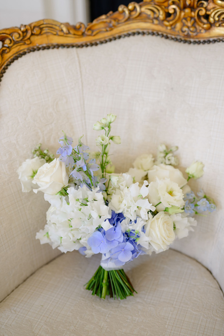 Elegant wedding bouquet with white and light blue flowers, placed on a vintage chair at Chateau Mcely