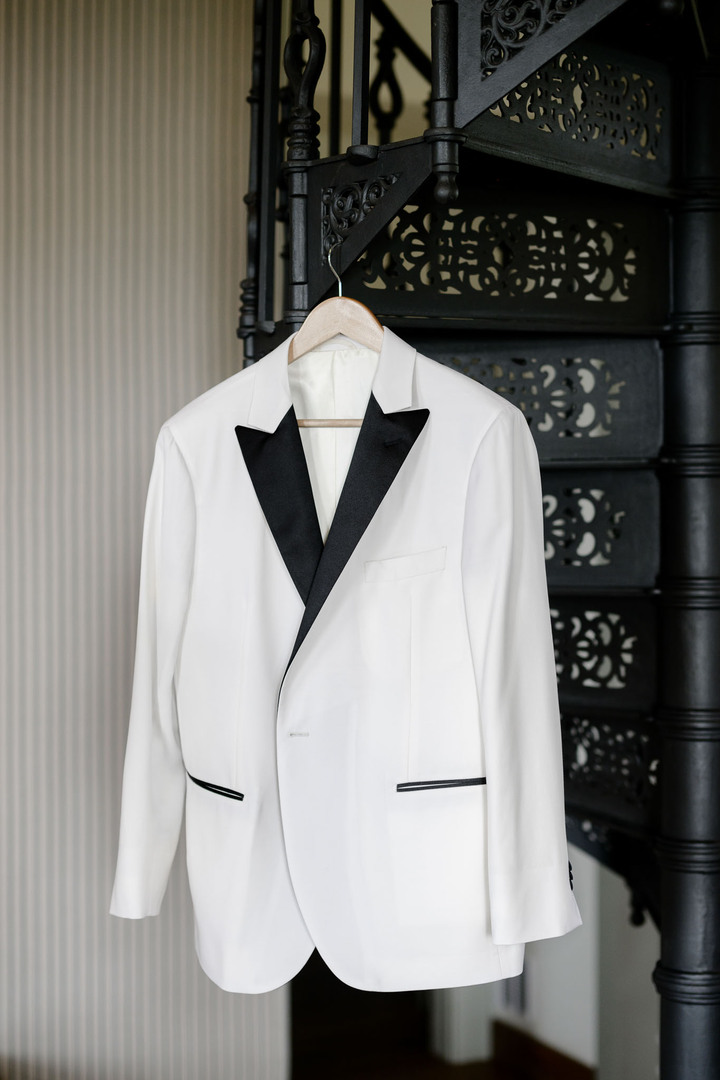 A white tuxedo with black lapels elegantly displayed on a hanger at a luxury chateau wedding.