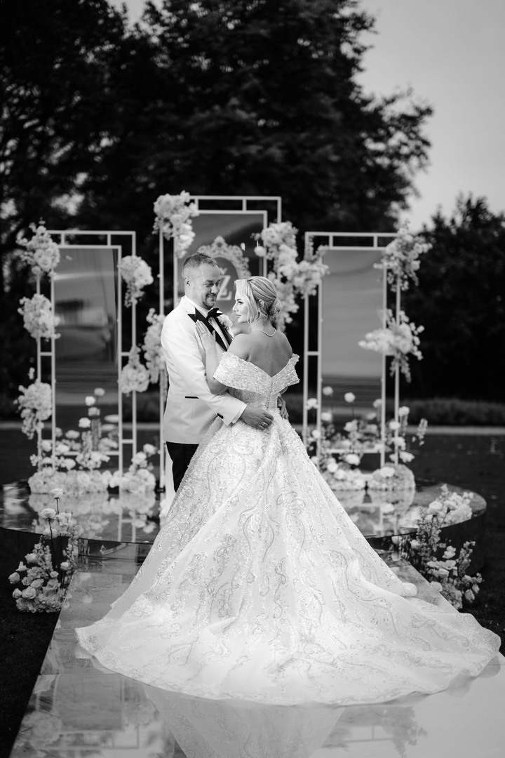 Romantic black and white photograph of a bride and groom embracing in front of an elegant floral archway at Chateau Mcely.