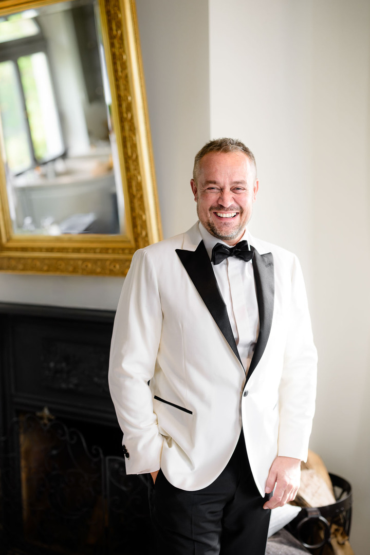 Groom in a white tuxedo in the elegant interior of Chateau Mcely.