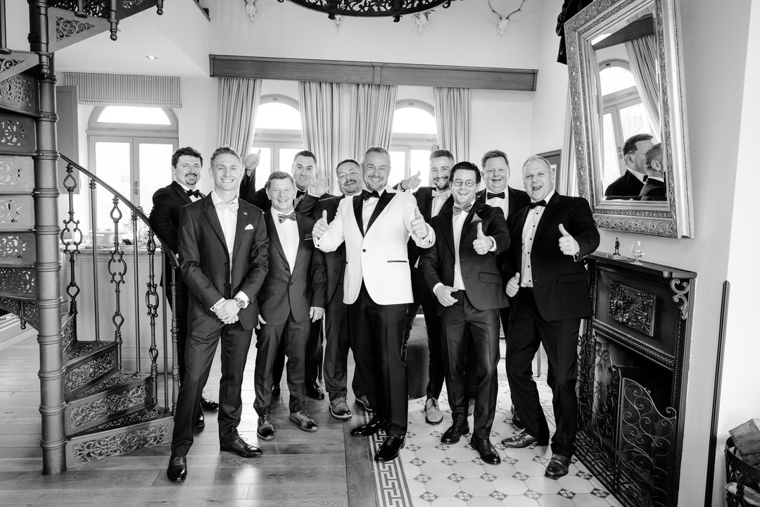 Groom and groomsmen posing together in formal attire, with the groom in a white tuxedo at a chateau wedding.