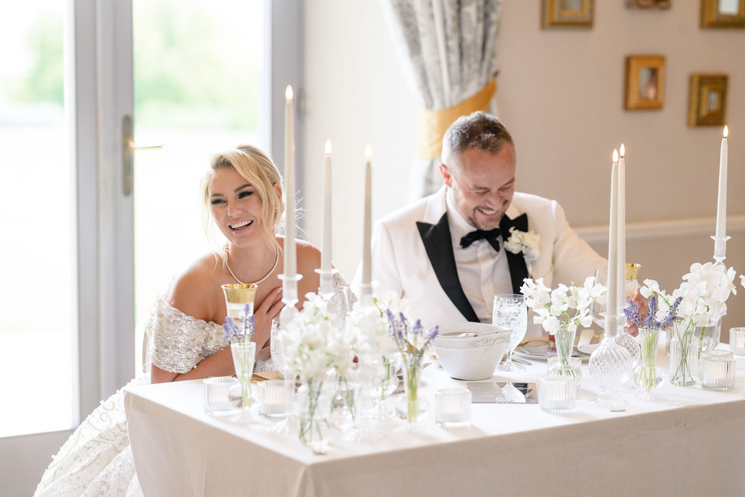 Bride and groom sharing a laugh at an elegantly set table with candles and flowers at Chateau Mcely wedding.