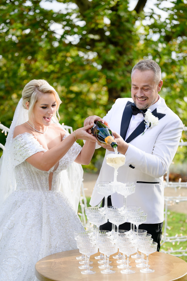 Bride and groom pouring champagne into a champagne tower at their luxurious Chateau Mcely wedding reception.