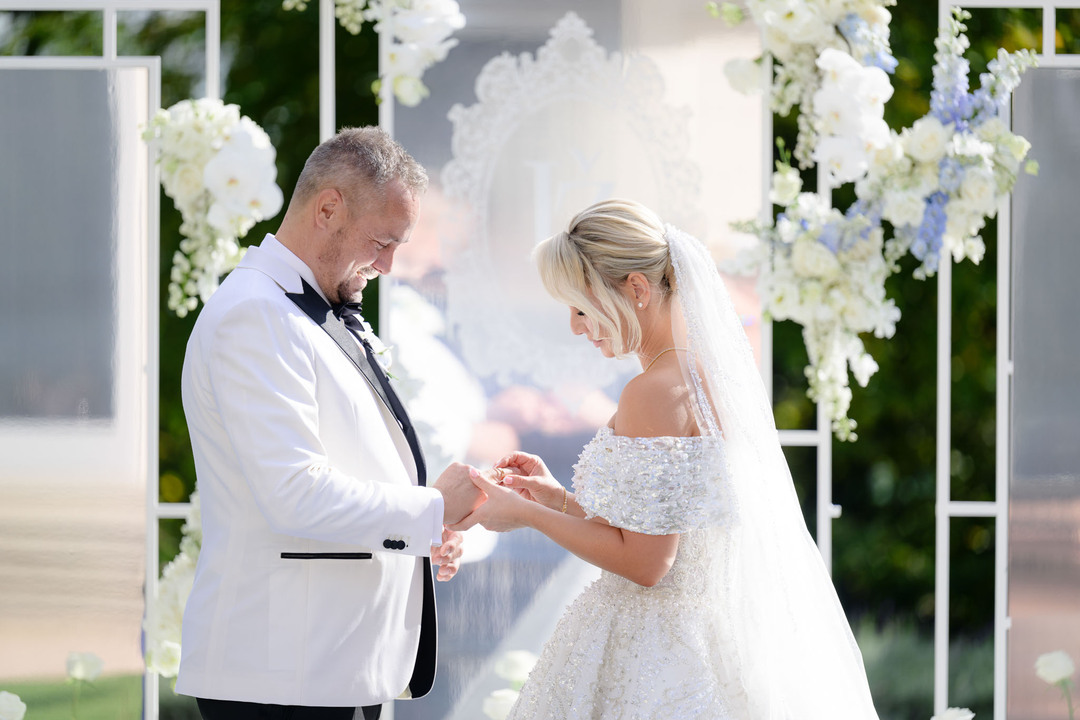 Bride and groom exchanging rings at a luxurious wedding ceremony at Chateau Mcely, surrounded by elegant floral decorations.