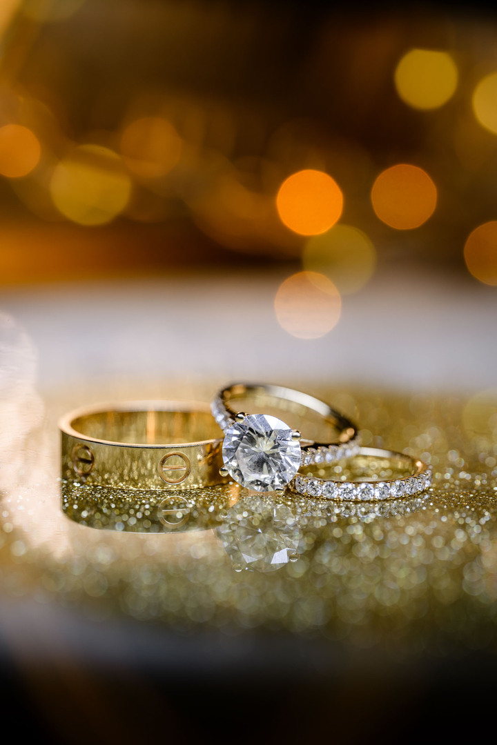 Close-up of exquisite wedding rings, including a Cartier band, set against a sparkling golden backdrop, capturing the essence of luxury.