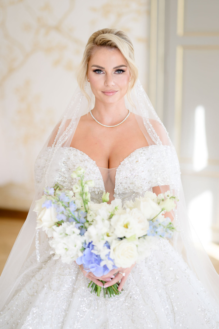 Stunning bride in a sparkling wedding gown holding a white and blue floral bouquet at Chateau Mcely.