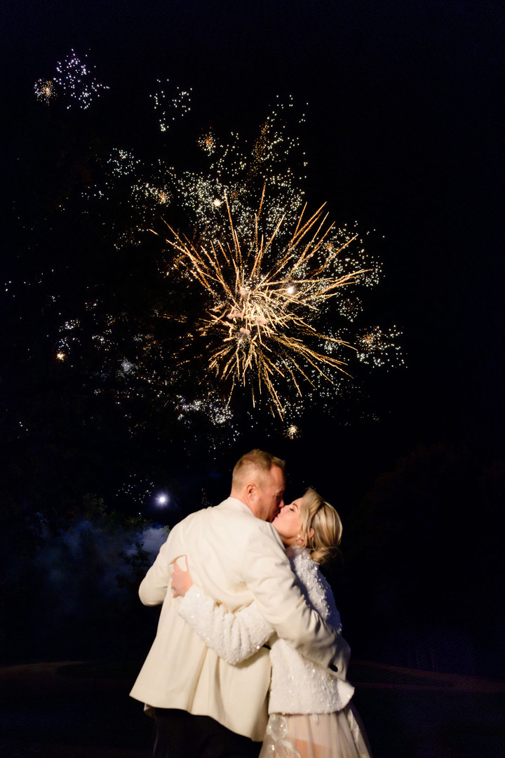 Bride and groom embracing each other while watching a spectacular fireworks display at Chateau Mcely, celebrating their special day.