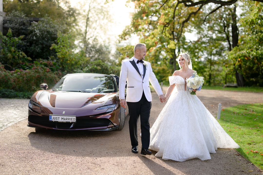 Nevěsta a ženich elegantně pózují před luxusním autem na Chateau Mcely.