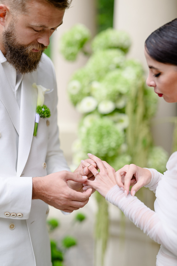 The groom places the wedding ring on fashion designer Debbie Brown during an intimate ceremony, surrounded by floral decorations.