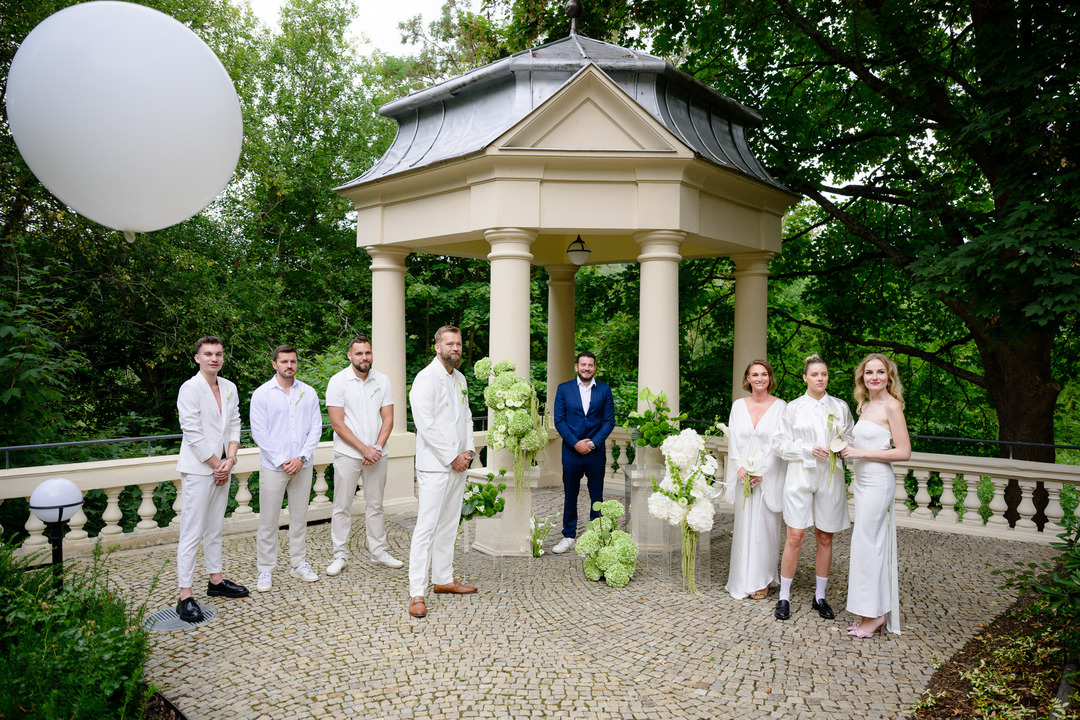 A wedding in Karlovy Vary – the groom in white is waiting for the bride. On the right, three bridesmaids are dressed in white, and on the left, three groomsmen are wearing white attire.
