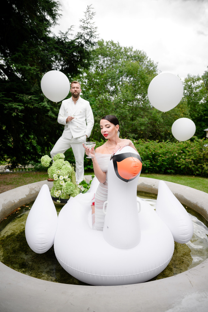 Bride Debbie Brown and the groom celebrate on an inflatable swan float by the fountain, surrounded by balloons and flowers.
