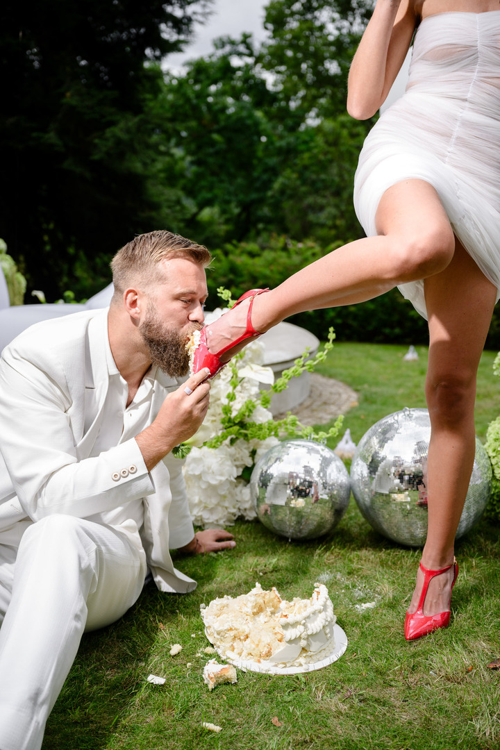 The groom licks the cake off the bride's high heel.
