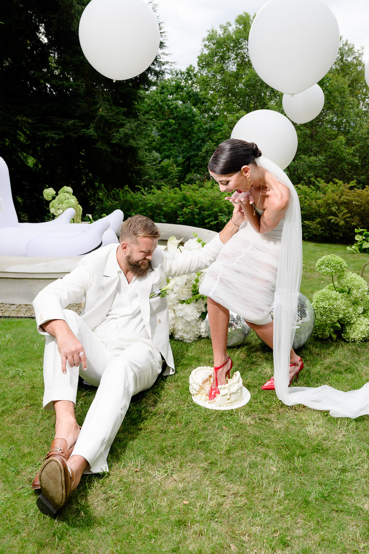 Fashion designer Debbie Brown steps on the wedding cake, while the groom smiles and watches.
