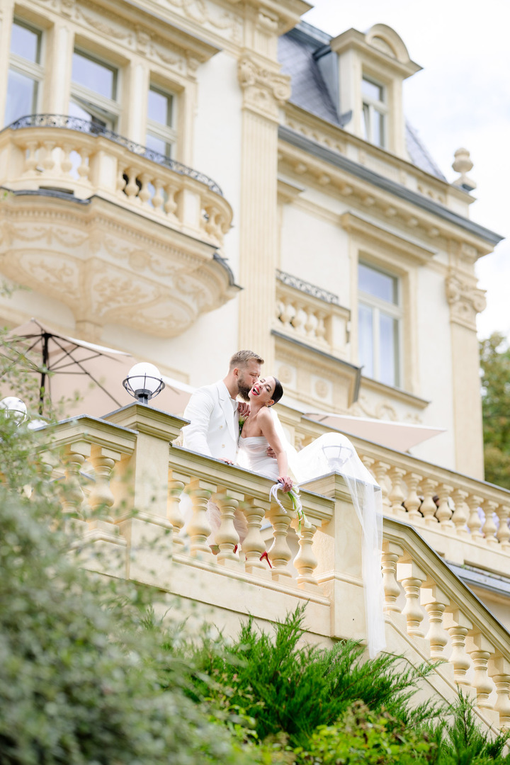 Happy newlyweds on the balcony of Villa Julius & Emma P. in Karlovy Vary, surrounded by elegant architecture and greenery