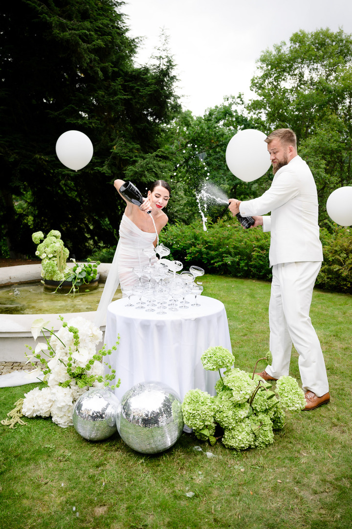 Debbie Brown and the groom together open champagne at the champagne tower in the garden of Villa Julius & Emma P., surrounded by balloons and disco balls.
