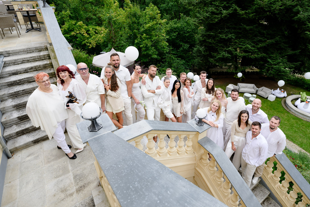 The newlyweds with their wedding guests – all dressed in white – stand on the staircase of Villa Julius & Emma P.
