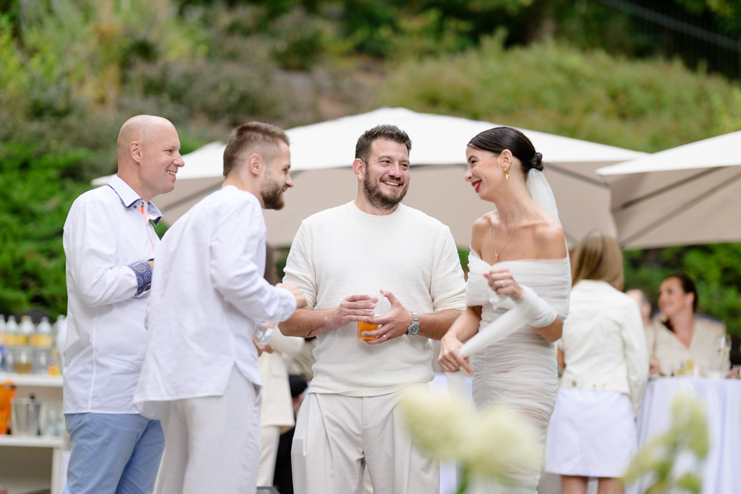 Debbie Brown's wedding in Karlovy Vary: The fashion designer laughs with guests during an outdoor celebration, surrounded by greenery and umbrellas.
