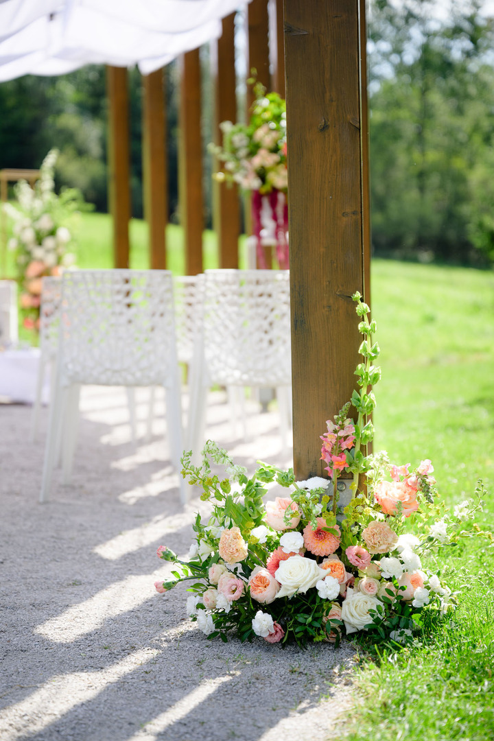 Details of the ceremony setup with white chairs and soft pink flowers for an summer wedding ceremony.
